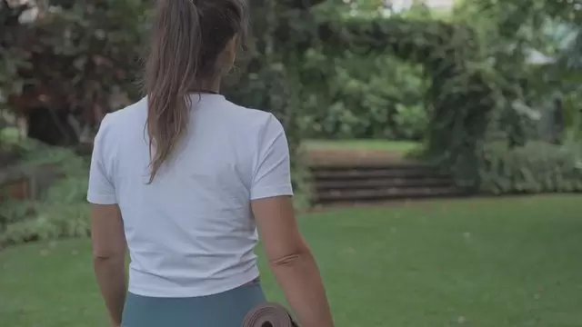 女人拿着瑜伽垫在公园散步视频素材插图
