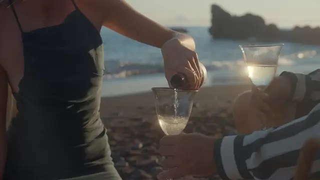 日落时分一名妇女在海滩上将香槟倒入玻璃杯中视频素材插图