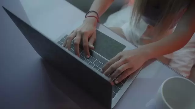 一个女孩坐在办公桌前，在笔记本电脑上打字视频素材插图
