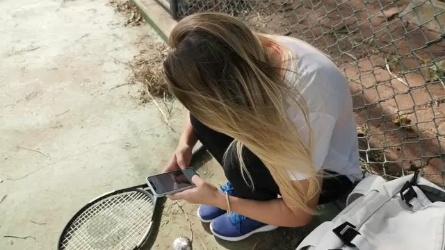 一名妇女坐在网球场上使用手机视频素材插图