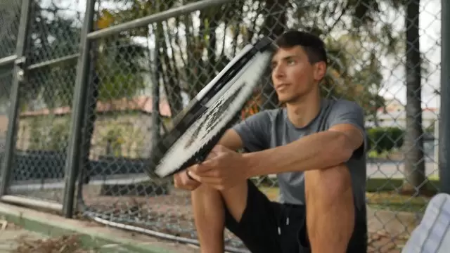 男子坐在地上旋转网球拍视频素材插图