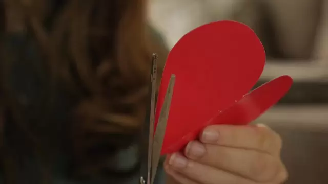 女孩用剪刀剪红色的纸心视频素材插图